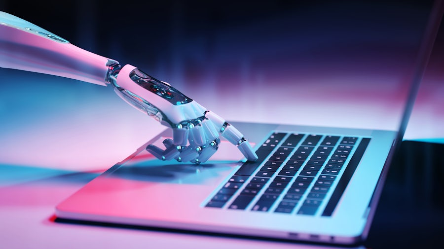 A robotic hand presses a key on a laptop computer keyboard.