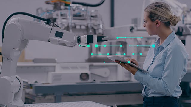 Female engineer working on a tablet in factory with a robotic arm.