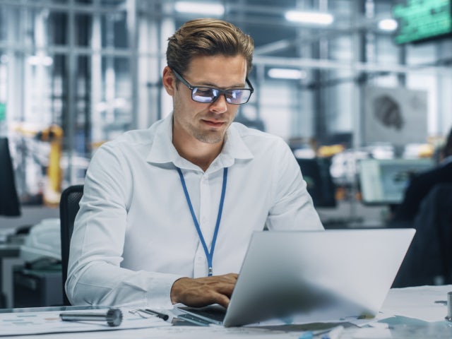 A man wearing glasses sits at a deck looking at a laptop.