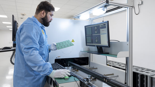 Engineer is working in a factory with a monitor in front of him and hardware chip in his hand