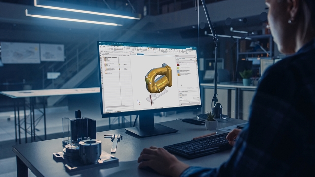 Engineer working on a desktop computer with Siemens' NX CAD modeling software displayed on the screen. She is designing a jigsaw arm and she has HD3D Visual Reporting open with sustainability calculations of her material selections.