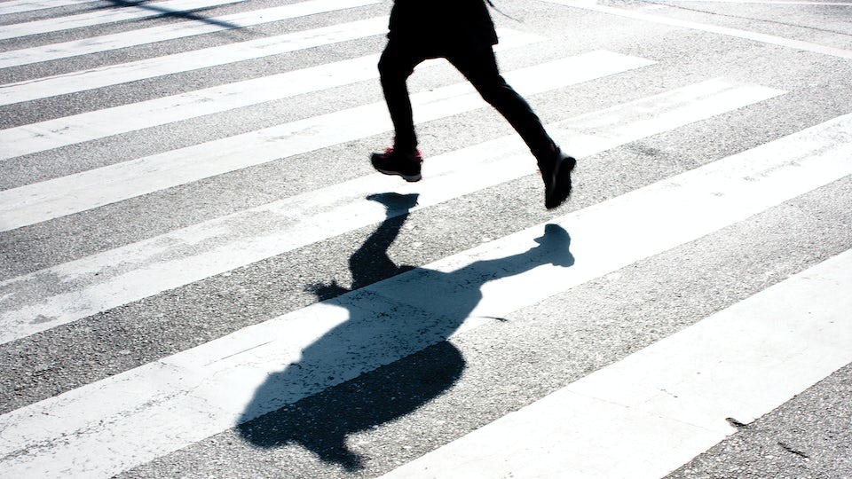 The legs and shadow of a person running across a crosswalk