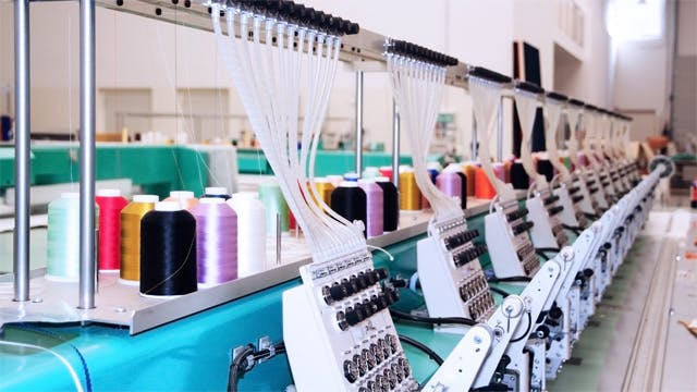 An industrial textile machine with multiple spools of thread of varying colors.