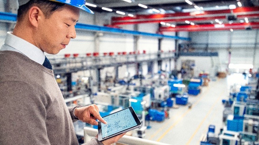 Un produttore utilizza un tablet con soluzioni di smart manufacturing mentre si affaccia sulla fabbrica.