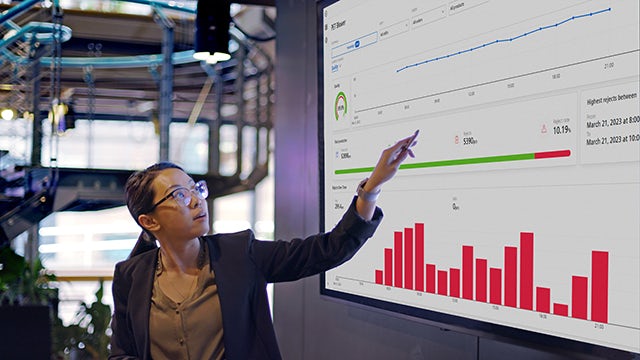 Woman standing in front of a large screen pointing at charts and graphs displayed.