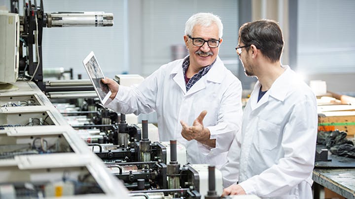 Image of two men in white lab coats in a factory or laboratory setting. One man is holding a tablet. The image is intended to illustrate the concept of managing quality inspections.