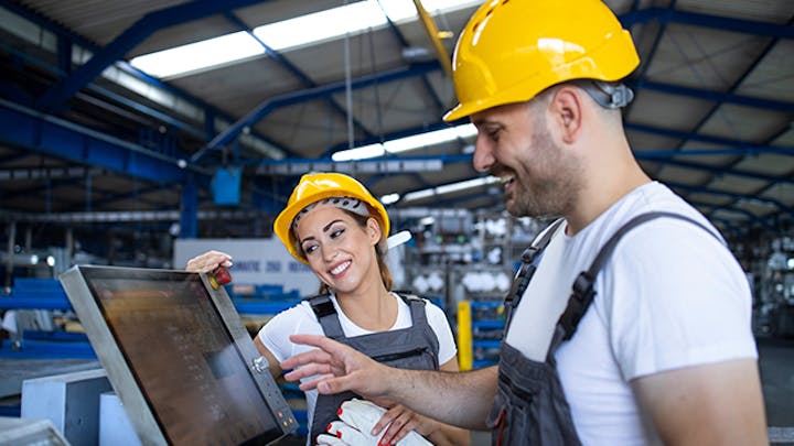 Image of a man and woman wearing yellow hard hats, working in a factory. The man is interacting with a computer monitor while the woman looks on. This image is meant to illustrate the concept of Statistical Process Control (SPC) in quality management.