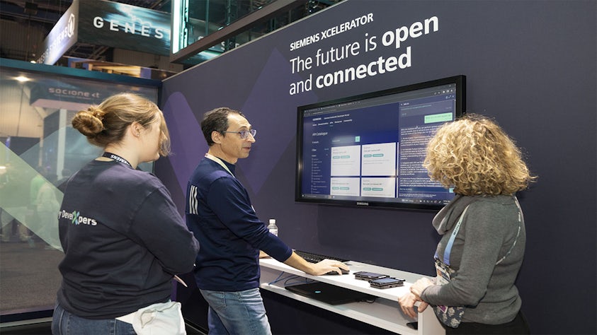 At the Consumer Electronics Show (CES), three people discuss a demo at the Siemens Xcelerator booth.