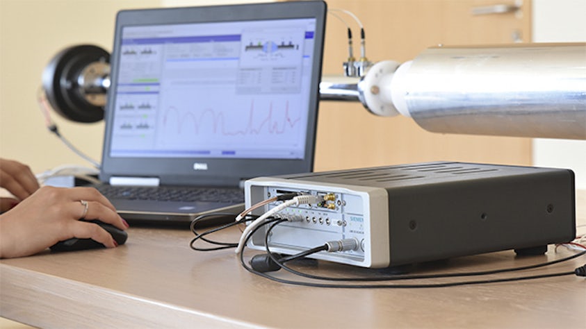 An engineer using a laptop and a Simcenter SCADAS device to identify acoustic material testing properties.