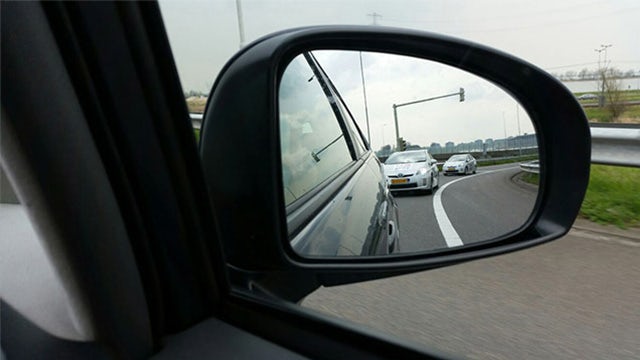 Autonomous vehicles on a test track, seen in the side mirror of another car