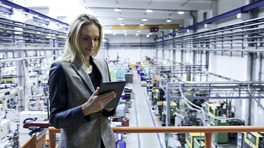 Person on a factory floor, looking at a tablet.