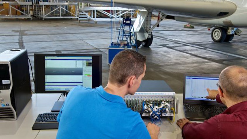 Zwei Ingenieure, die ein Experiment auf einem Computer in einem Flugzeughangar durchführen