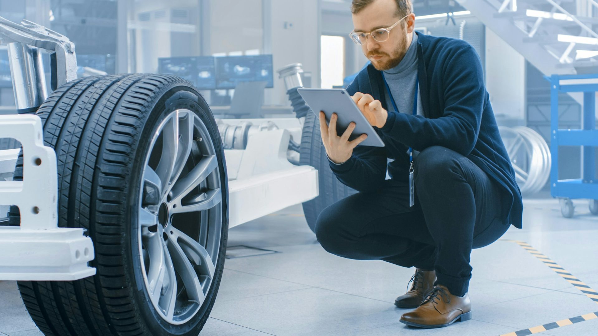 A man kneels in front of a tire as he looks at information on a tablet computer