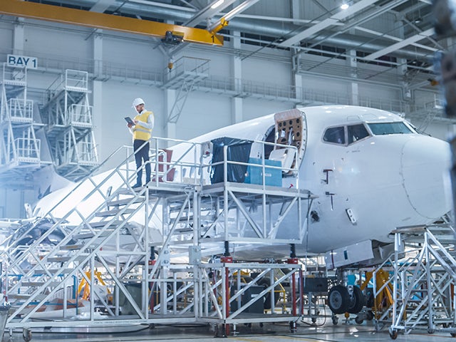 Engineer in a safety vest standing beside an airplane in a hangar, using the Questa One DO-254 safety solution.