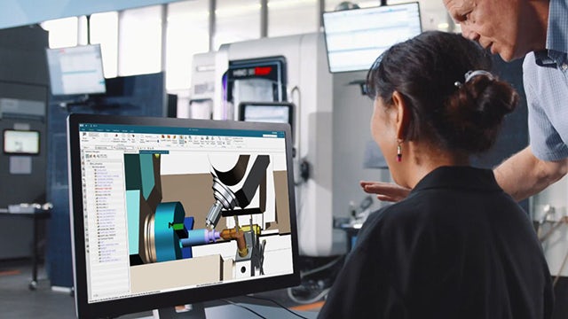 Uomo e donna in uno stabilimento di produzione che guardano NX sullo schermo di un computer