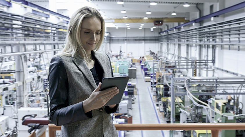 A woman standing in a factory using a tablet.</br>	