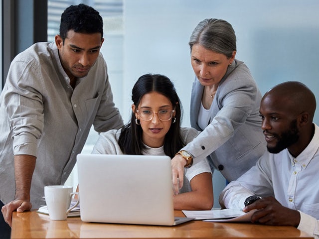 Four co-workers looking at a laptop screen with one pointing at the monitor.