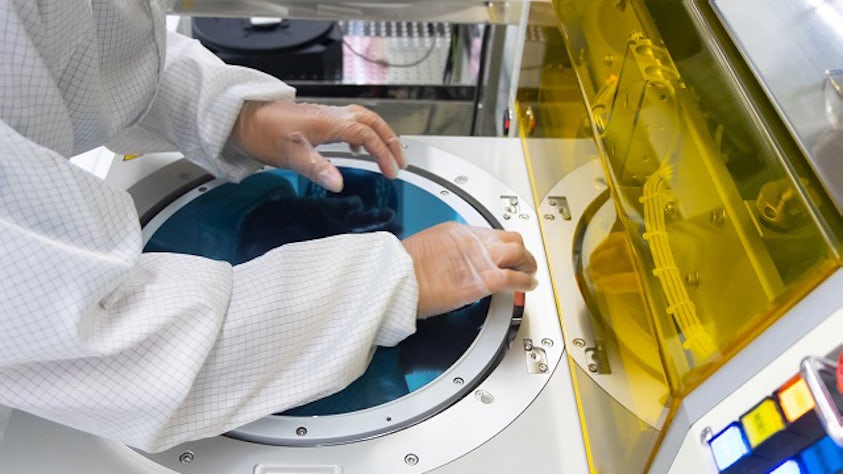 Una persona en un laboratorio que lleva guantes y está trabajando en la fabricación de semiconductores.