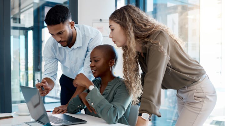 3 人のチーム メンバーが一緒にコンピューターで作業しています。