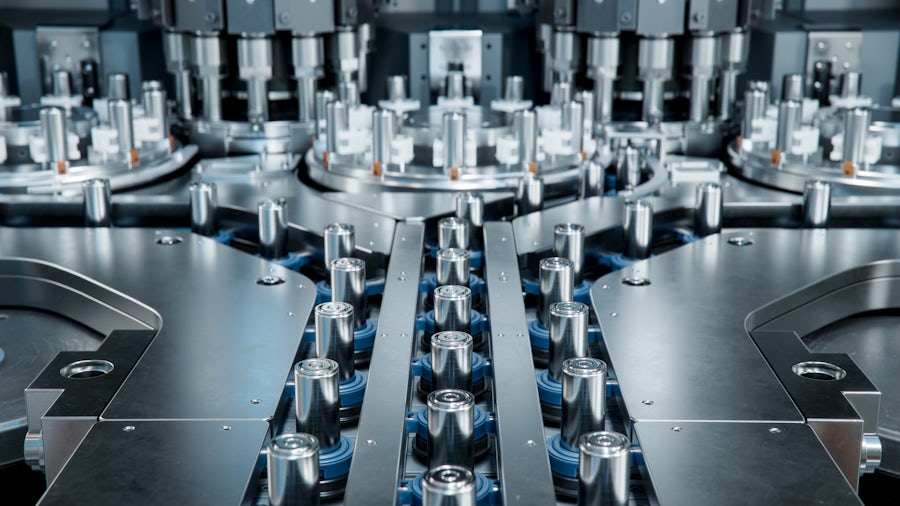 Silver battery cells on a stainless steel conveyer belt moving through the production floor.