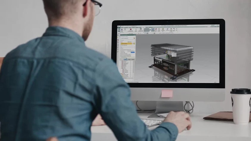 Man working at a desk with a desktop computer displaying a 3D model in Siemens software, representing digitalization in product design and engineering.