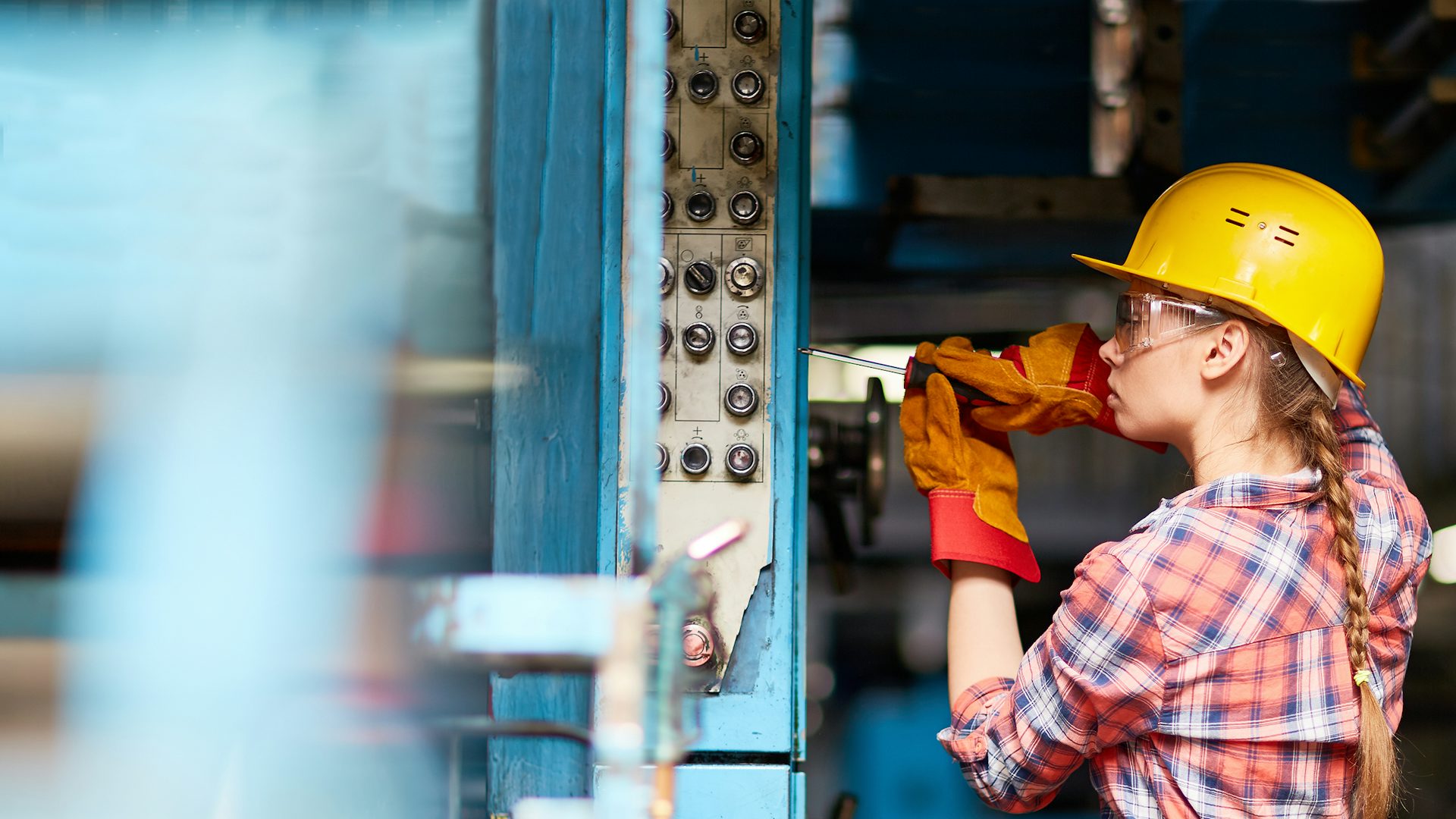 Female worker wearing a hardhat, safety glasses and gloves performing work in a factory.