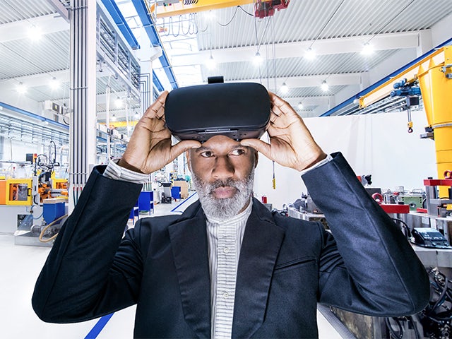 Responsabile di produzione con cappotto nero che utilizza un visore per la realtà virtuale in fabbrica.
