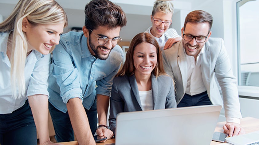 Group of business people standing around a laptop smiling.