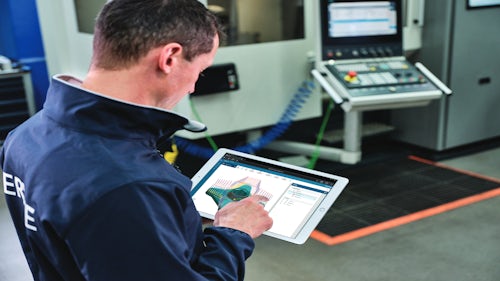 An engineer on a machine shop floor looking at performance testing results on a tablet.