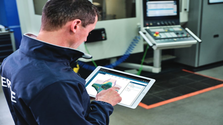 An engineer on a machine shop floor looking at performance testing results on a tablet.