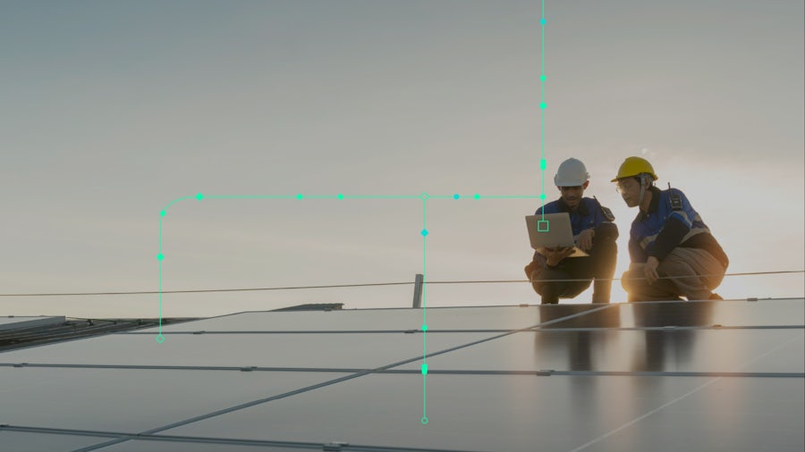 Two technicians kneeling next to solar panels looking at laptop computer.