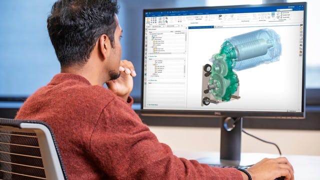 A man sits at a computer, creating a digital model of a machine part