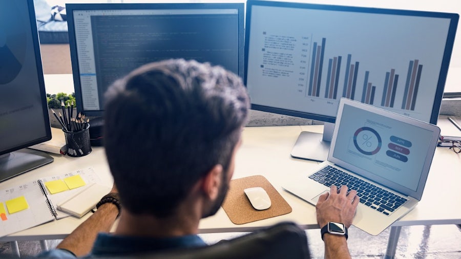 Un homme travaille sur la conception de logiciels embarqués simultanés intégrés, son ordinateur portable et ses moniteurs affichent des graphiques et des logiciels de conception de batteries