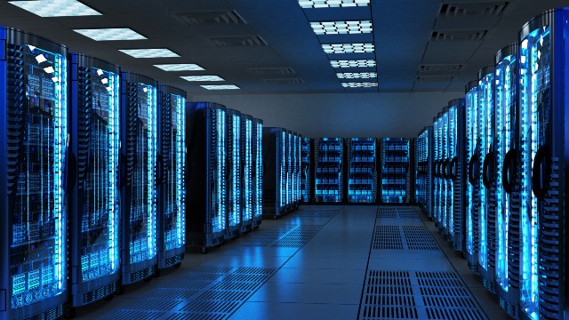 A futuristic data center with rows of illuminated server racks glowing with blue lights. The room has a sleek, modern design with a reflective floor and overhead lighting, emphasizing the high-tech environment.