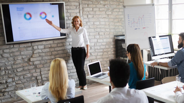 A session where an instructor is explaining on a large screen and attendees are sitting on their desks 