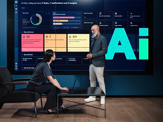 Two professionals review data on a large digital screen displaying system insights, with the Siemens shape, Ai, highlighting the focus on artificial intelligence.