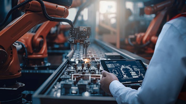 一个人看着平板电脑,而机械臂在装配线上组装零件