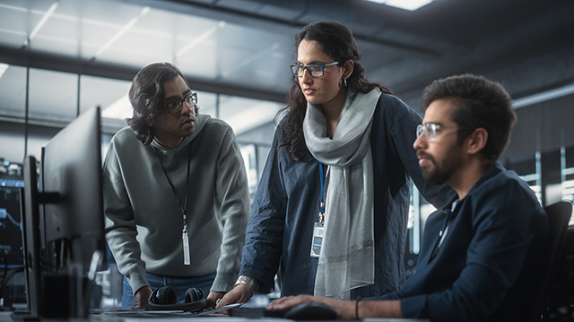 Tre dipendenti in piedi intorno a un computer in un ufficio.
