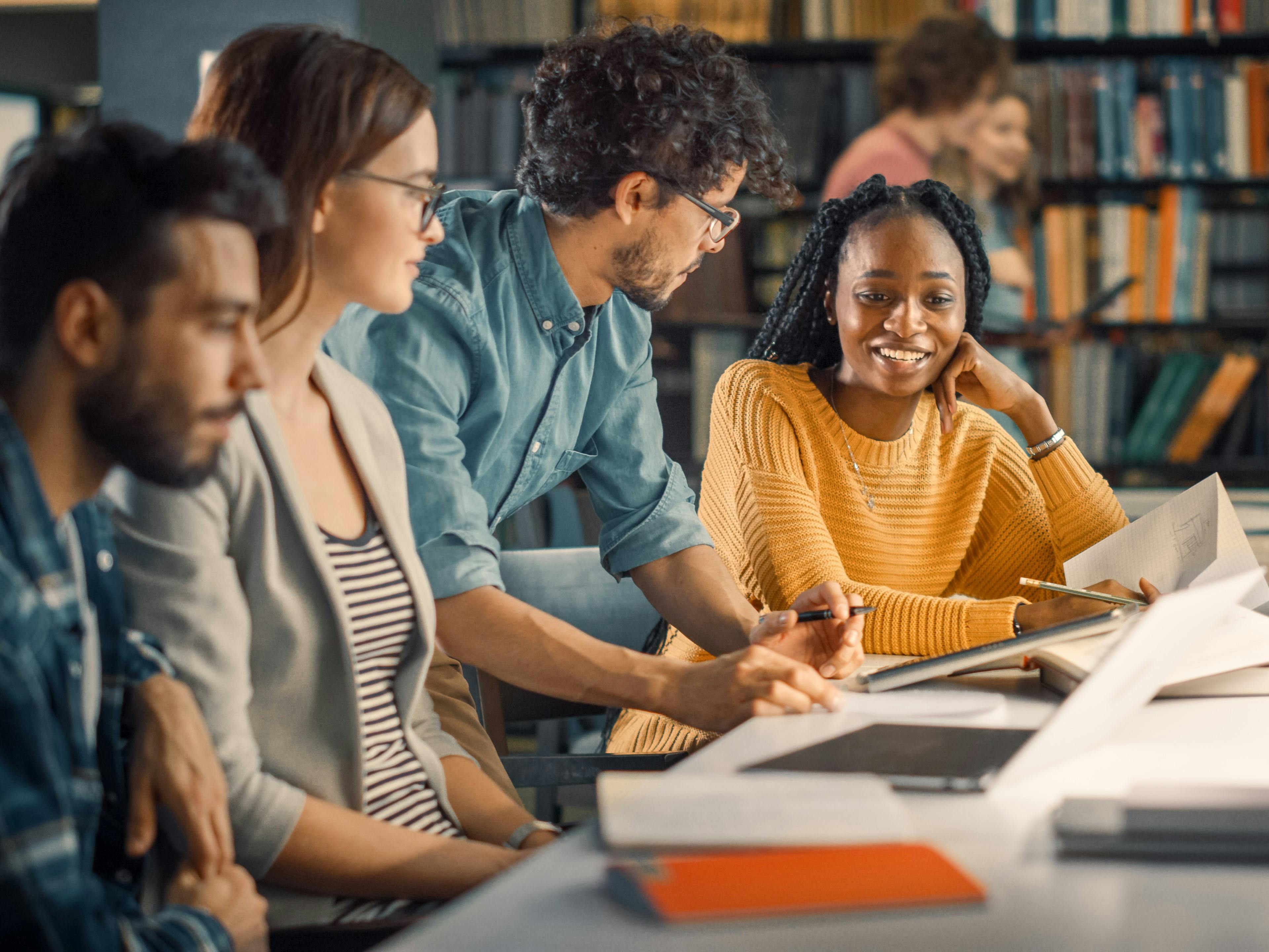 A group of students smile and study in a library.