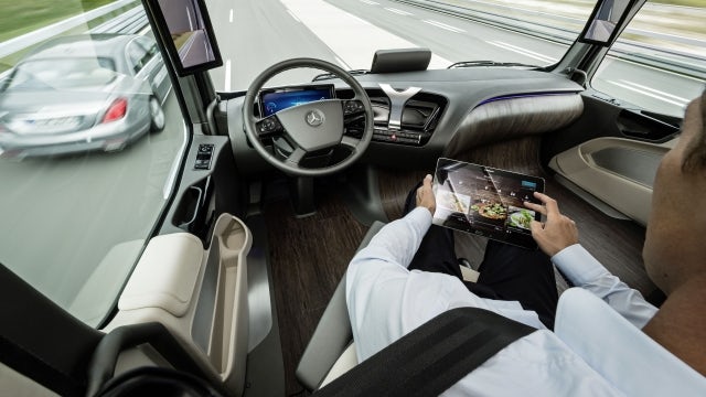 A man working on a tablet in the driver's seat of an autonomous vehicle on the road