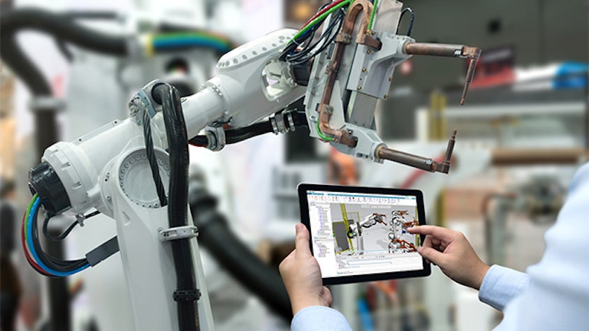Engineer holding tablet displaying 3D robotics simulation model in front of real robot on the factory floor.