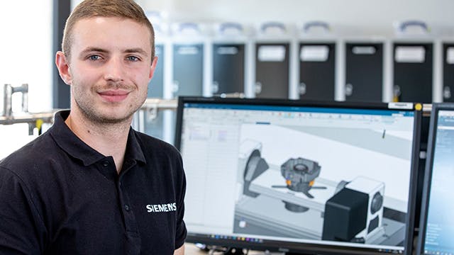 Man wearing a Siemens shirt smiling at the camera while sitting in front of a computer displaying a 3D model of a machine component in Siemens digital twin software.